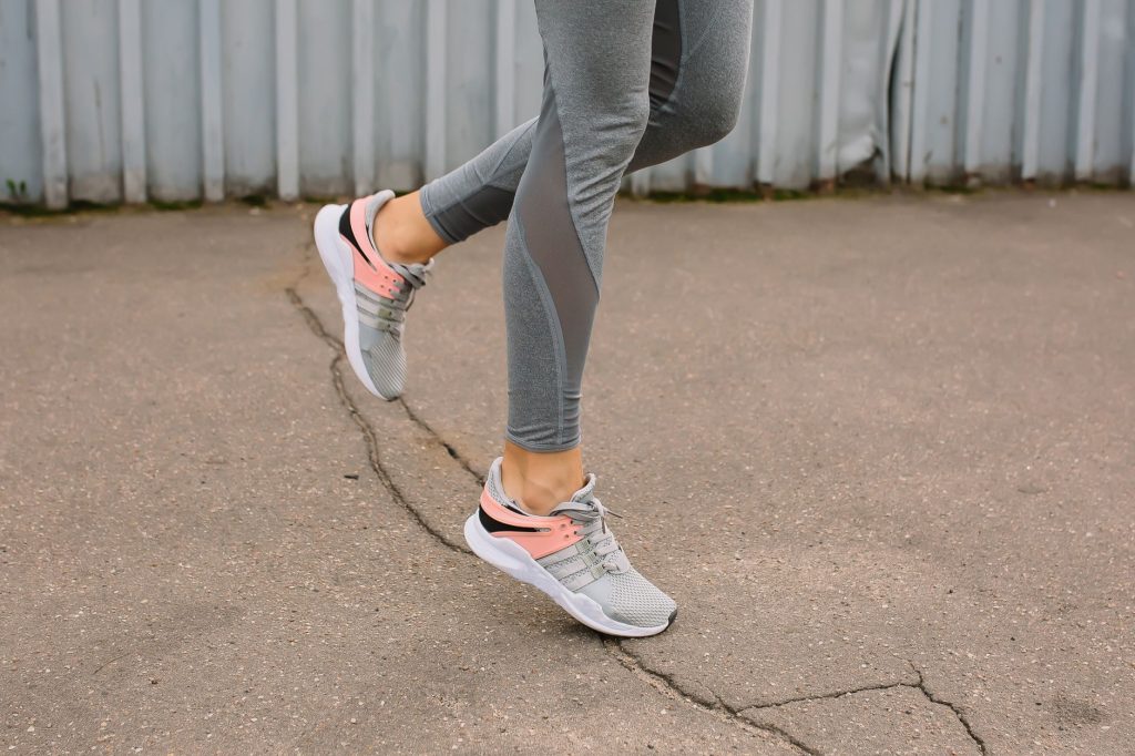 Close-up of a woman running on pavement in gray leggings and sneakers.