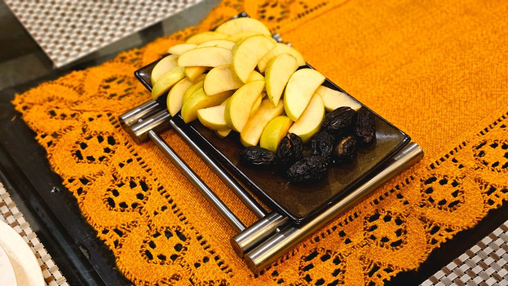 Sliced apples and prunes on a sleek black platter over a vibrant orange lace tablecloth.